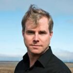 Photo of bestselling author Amy Weir with windblown hair and a black button shirt with desert background