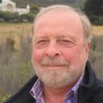 Photo of bestselling author Nelson DeMille smiling, wearing a dark jacket, standing in a field